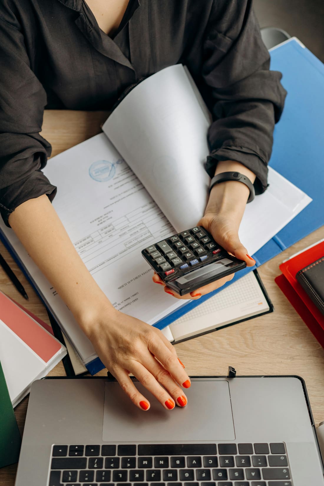A bookkeeper at a desk reviewing accounts with a calculator and laptop